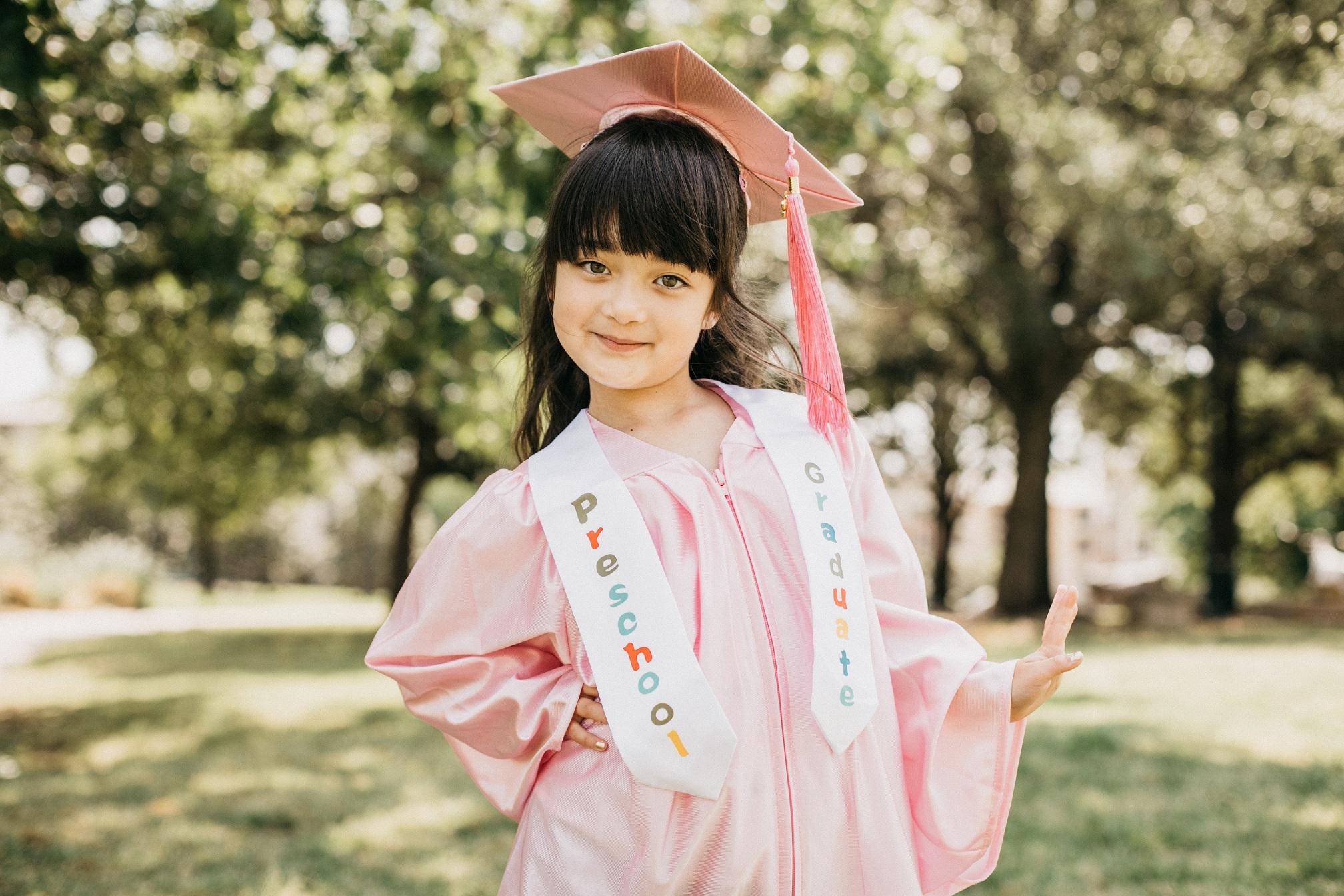 smiling girl with a graduation cap and ribbon posing for a photoshoot in a park