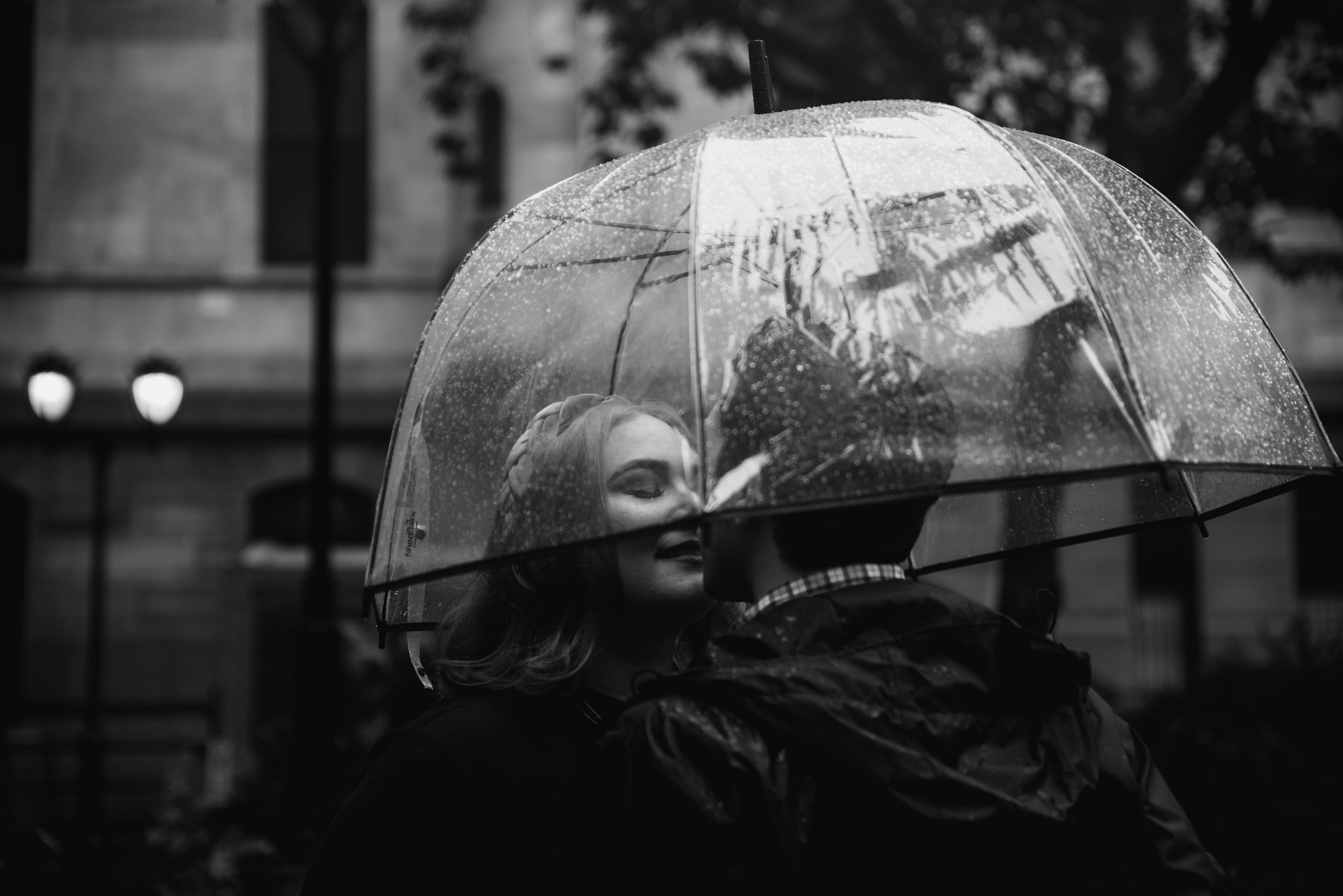 A couple embracing under a clear umbrella on a rainy day.