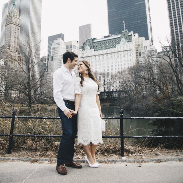 A couple holding hands and looking into each other's eyes in Central Park with skyline and trees in the background.