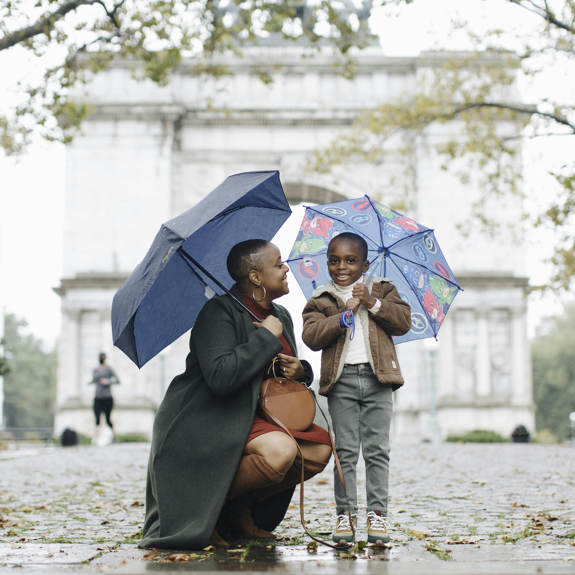 A smiling woman and a child holding umbrellas on a rainy day in front of a monument.
