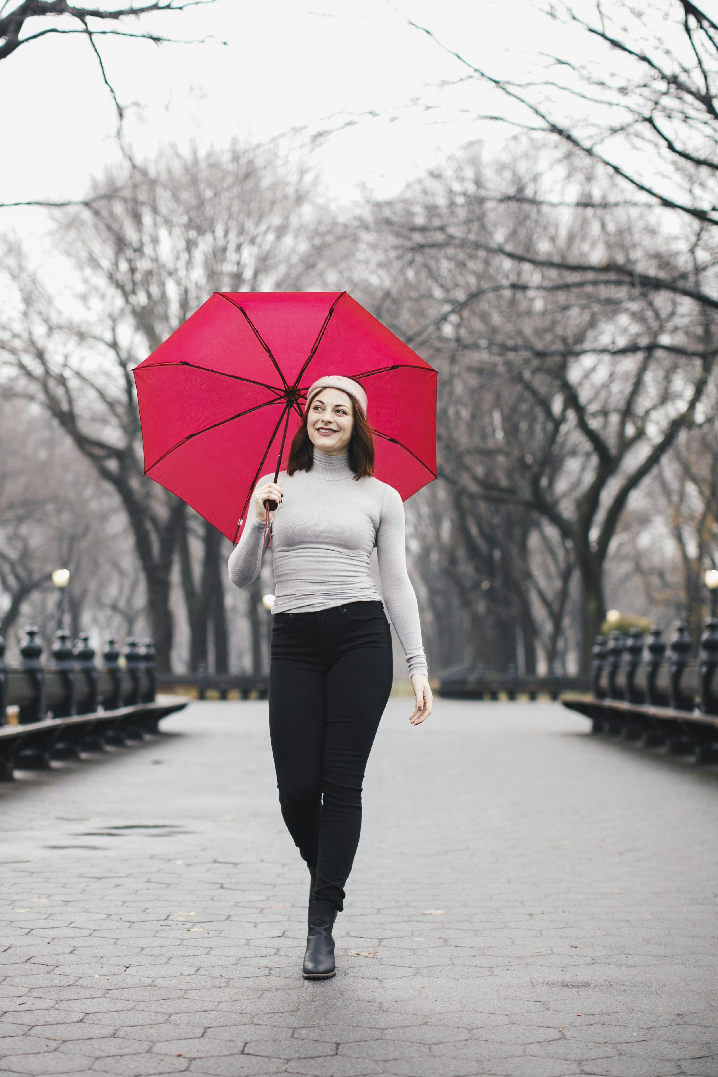 A woman walking with a red umbrella in a park.