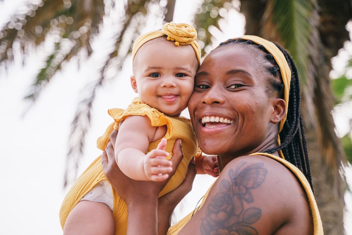 smiling mother holding up a toddler with a palm tree in background