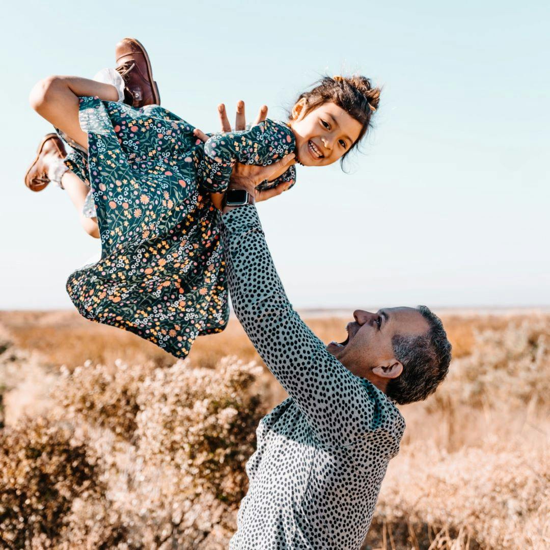 a father throwing his daughter in the air on a beach