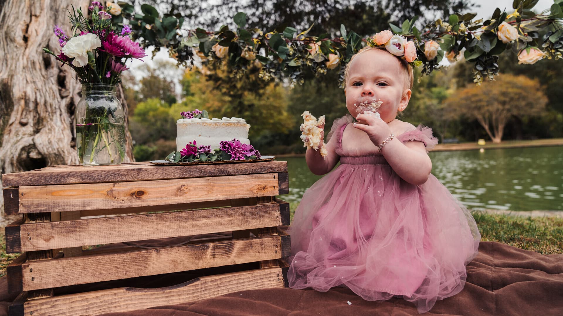 Baby girl in a pink tutu dress at an outdoor cake smash with floral decorations