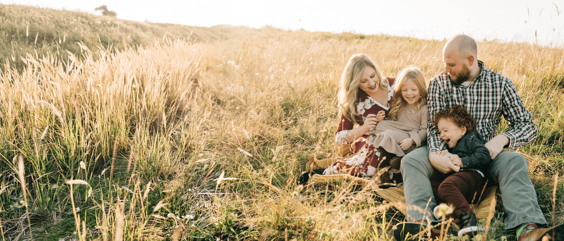 Family of four sitting together in a golden grass field
