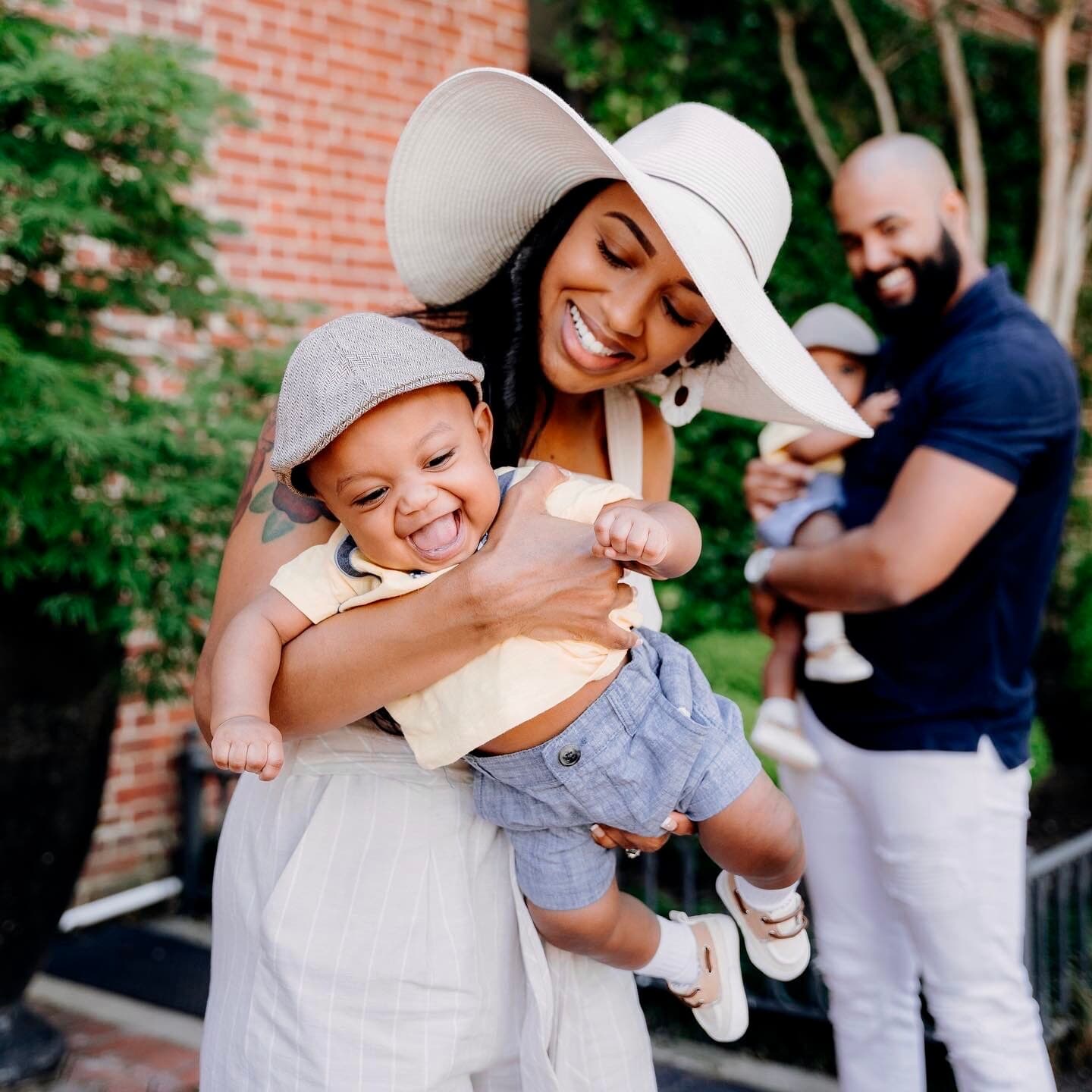 Mother holding a baby while a father stands in the background outdoors