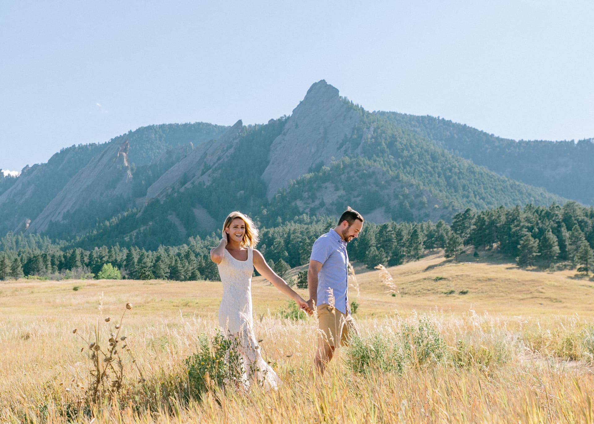 Couple holding hands walking through a golden meadow with mountain views