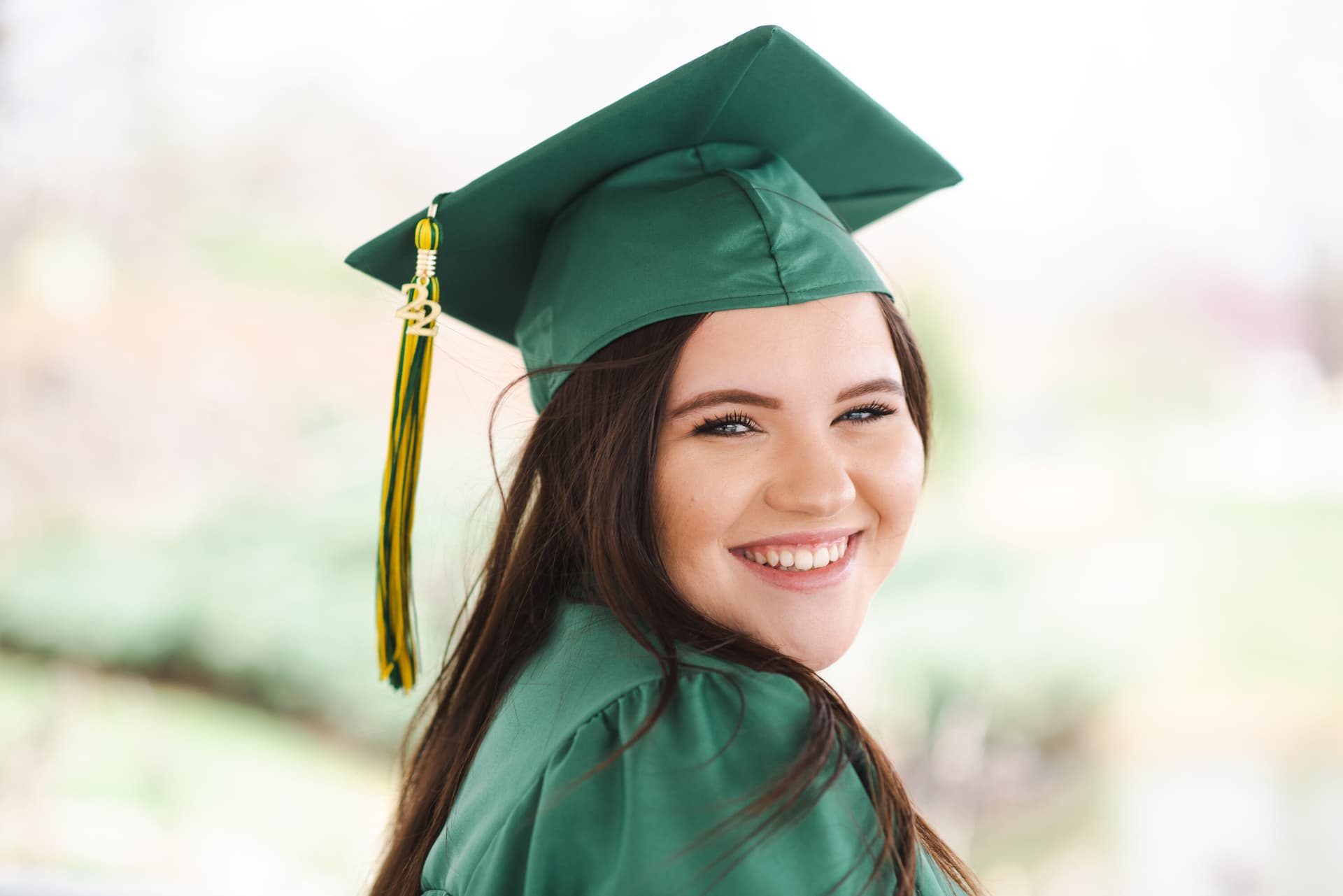 Young woman smiling in a green graduation cap and gown