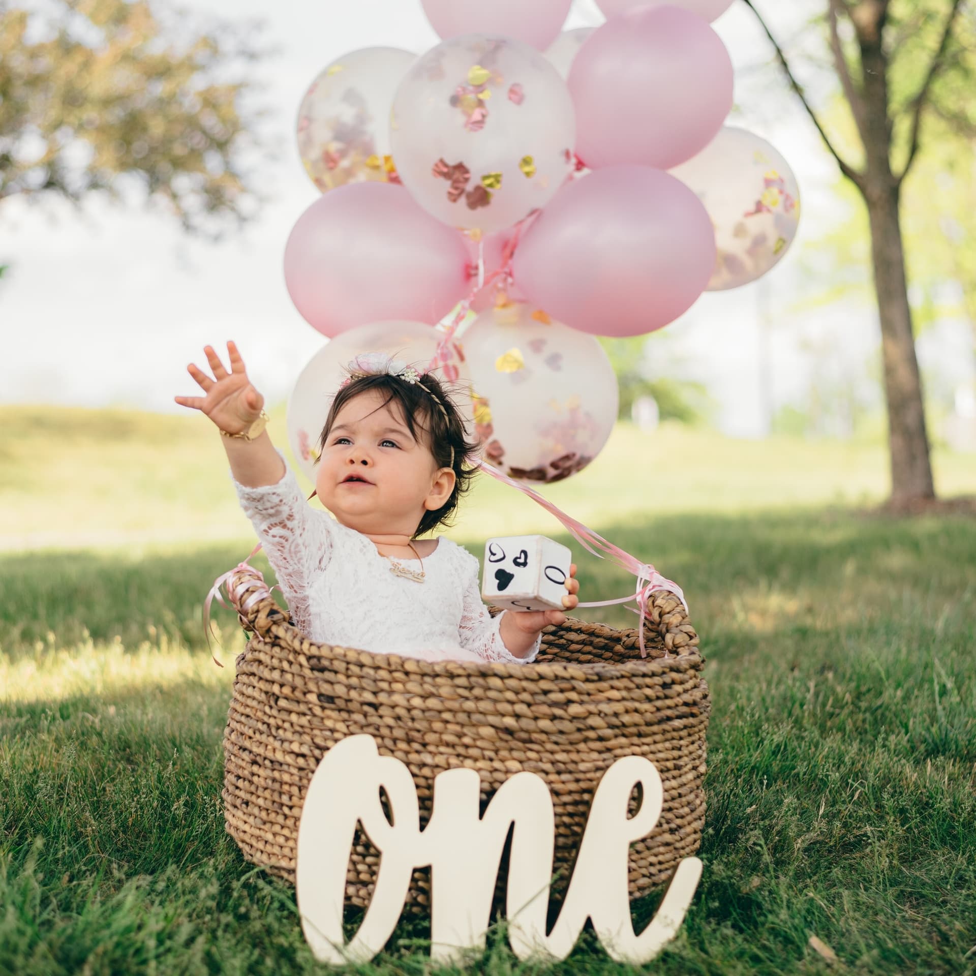Baby girl in a wicker basket celebrating her first birthday with balloons