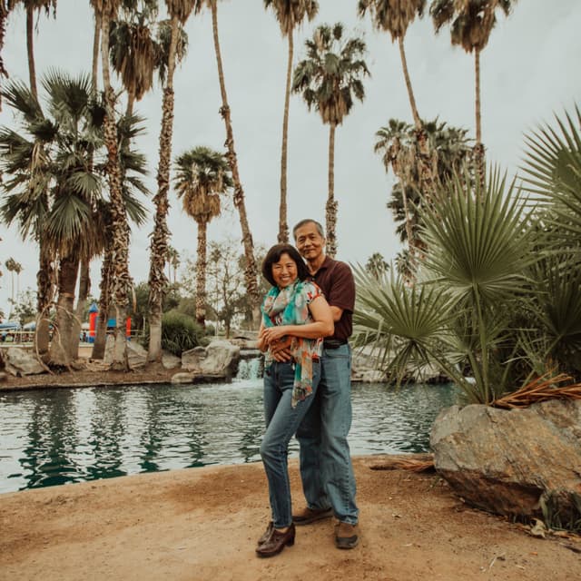 A couple hugging by a pond surrounded by palm trees and vegetation.