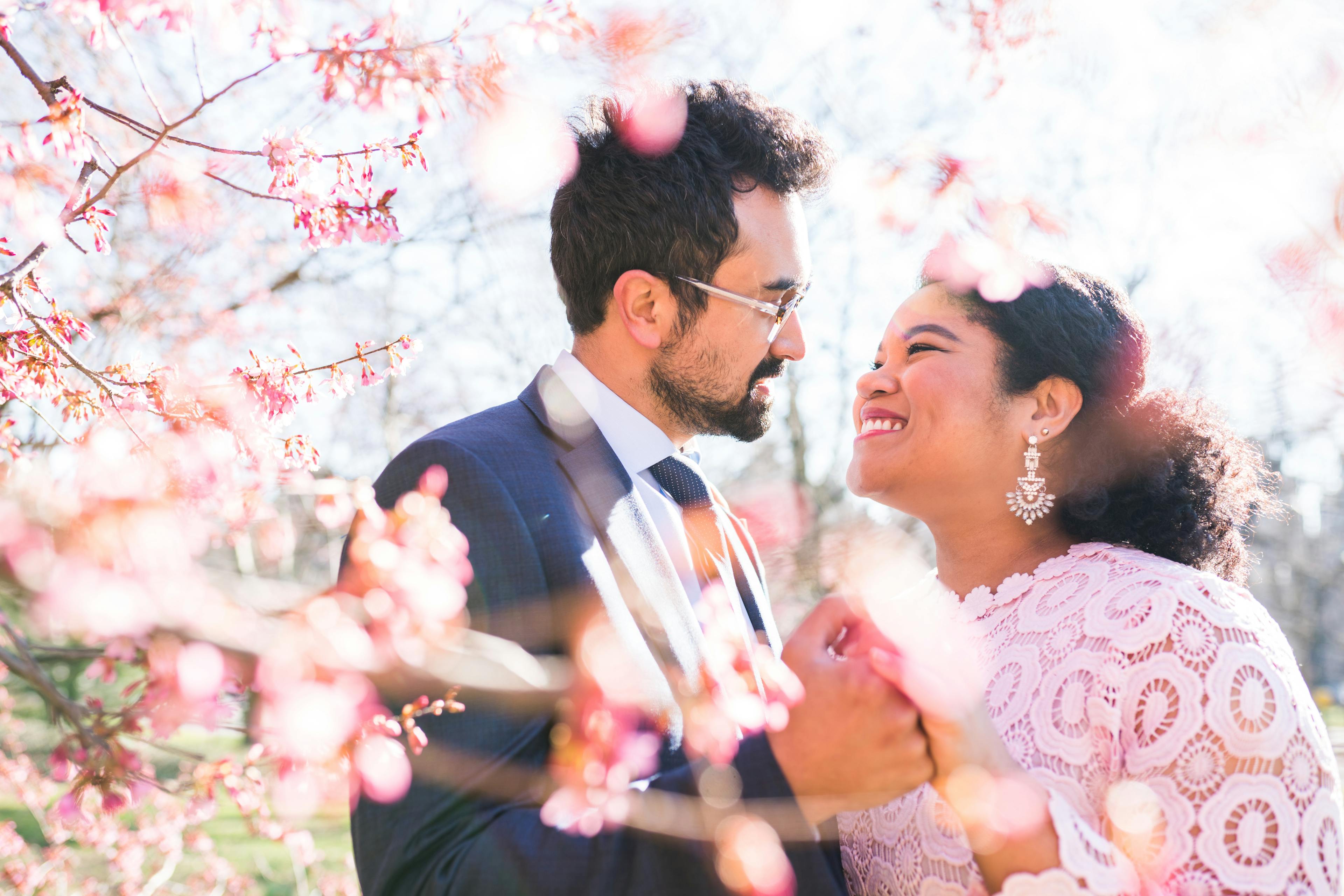 A smiling couple facing each other surrounded by pink blossoms.
