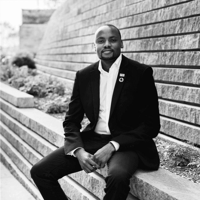 A black and white photo of a man sitting on steps wearing a suit and looking pensively to the side.