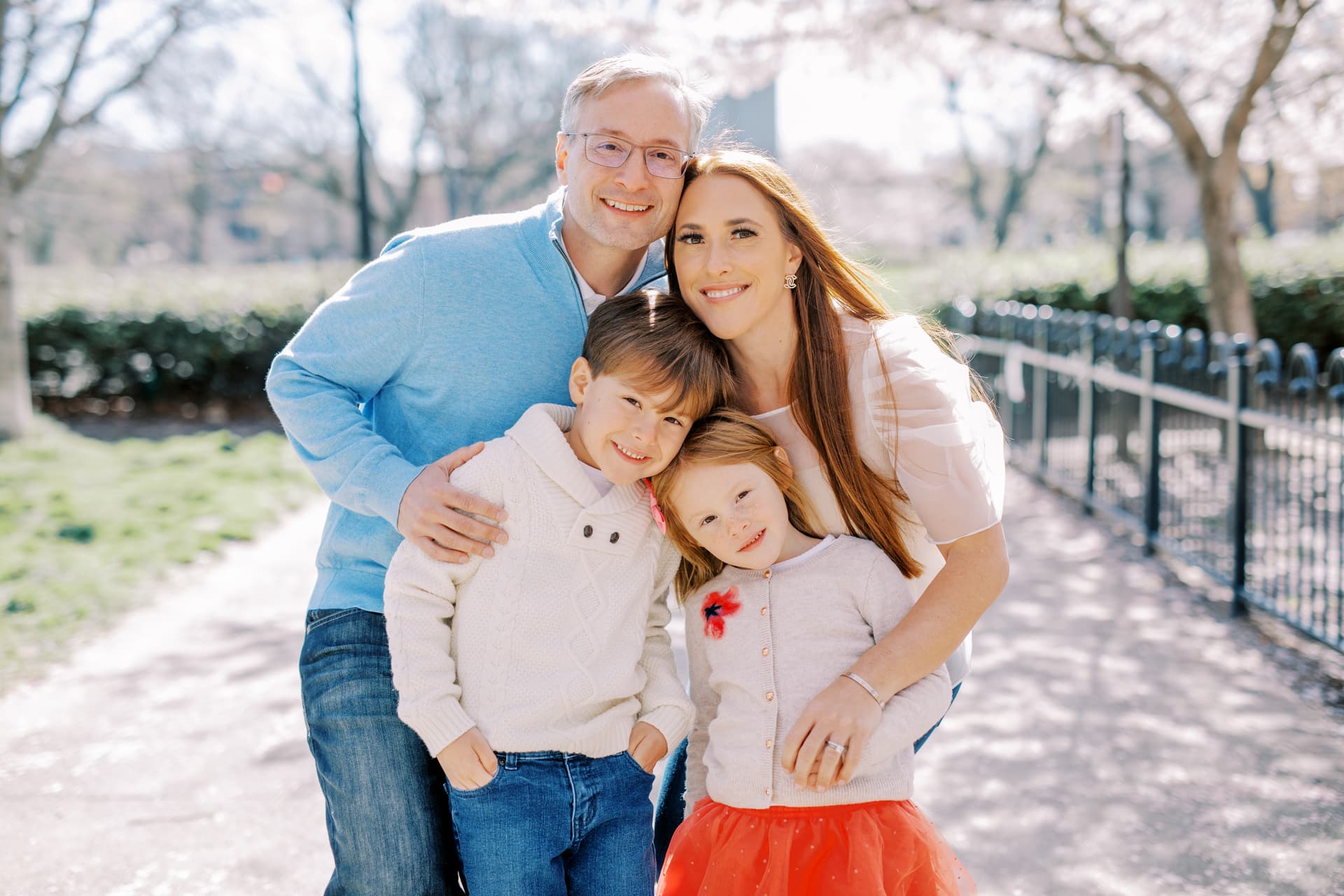 A happy family consisting of a man, a woman, and two children smiling outdoors on a sunny day.