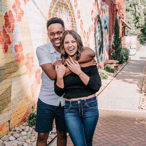 A joyful couple hugging each other with a colorful mural in the background.