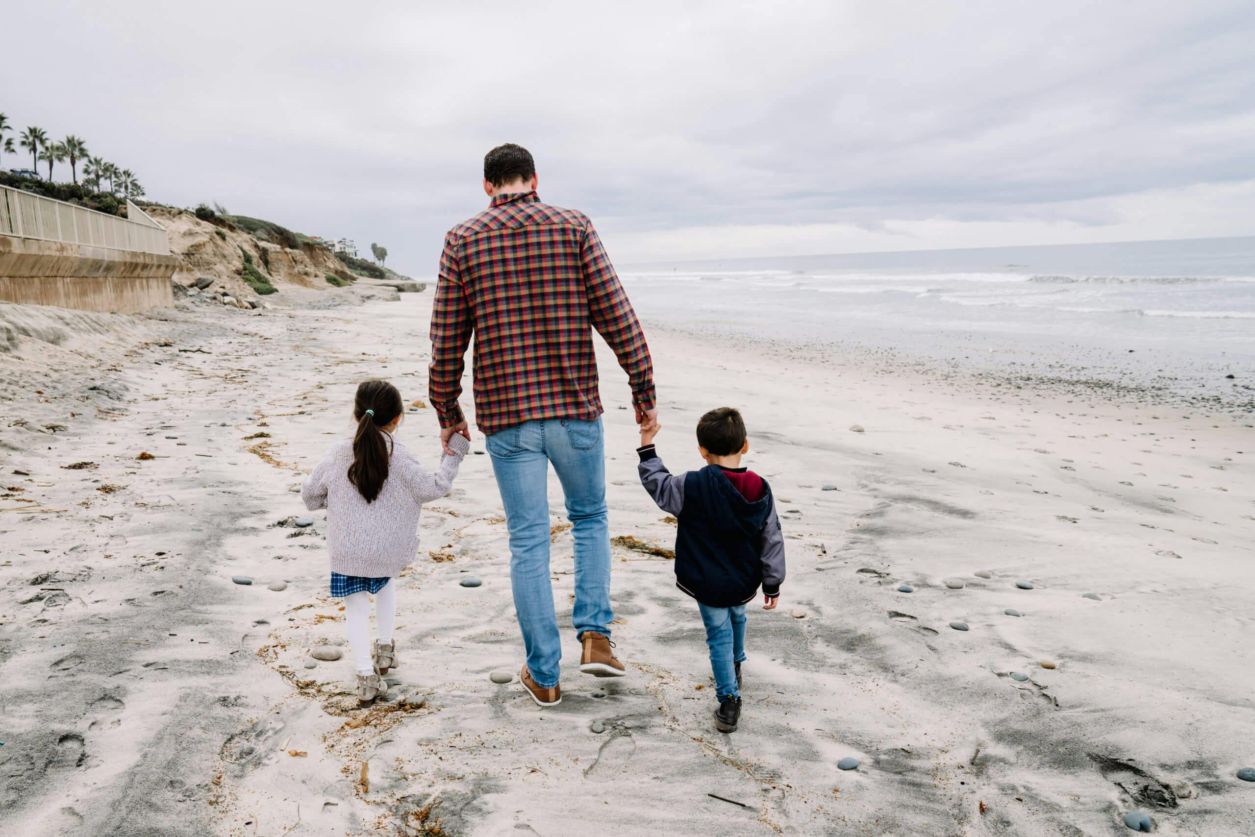 A man walking on the beach holding hands with two young children