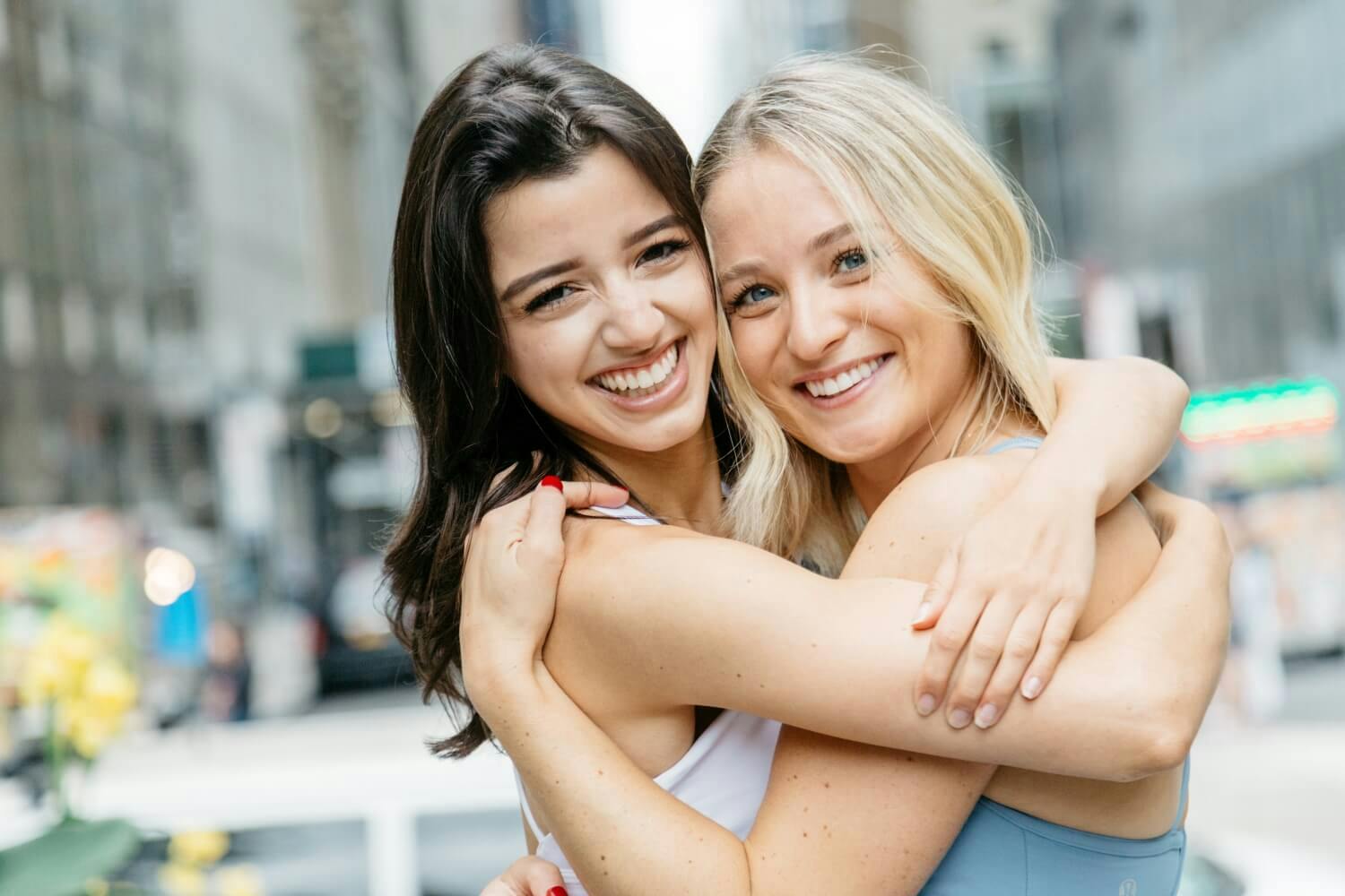 Two women smiling and embracing each other on a city street