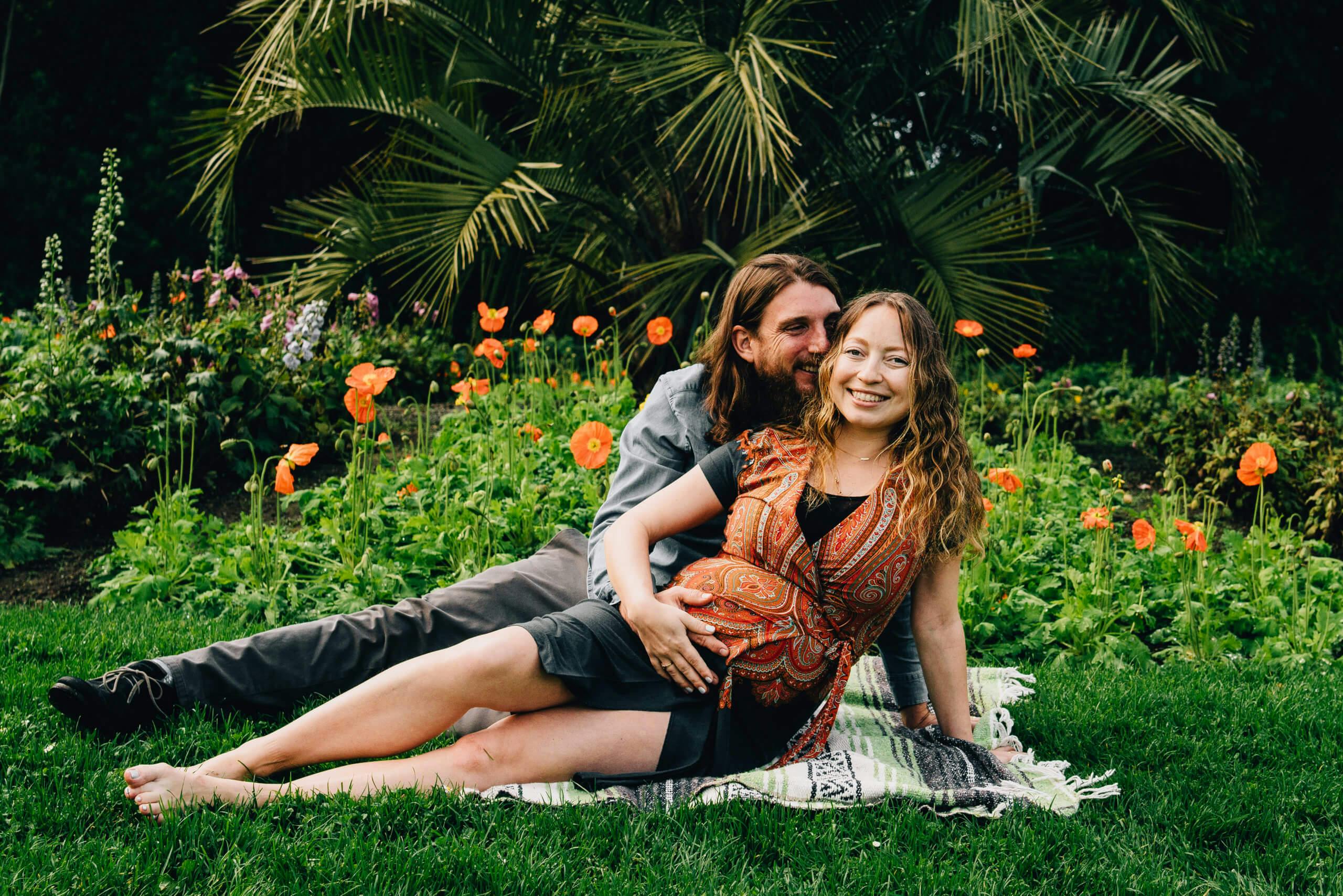 A couple lounging on a picnic blanket in a garden with orange flowers.
