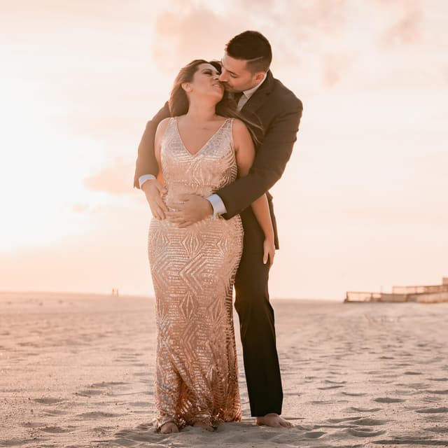 A couple on the beach at sunset, the man kissing the woman on her forehead