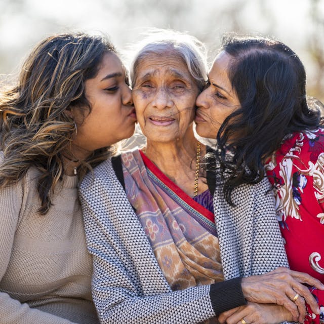 Three generations of women with the eldest being kissed on the cheek by the other two