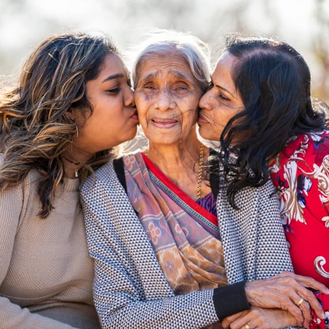 Three generations of women with the eldest being kissed on the cheek by the other two