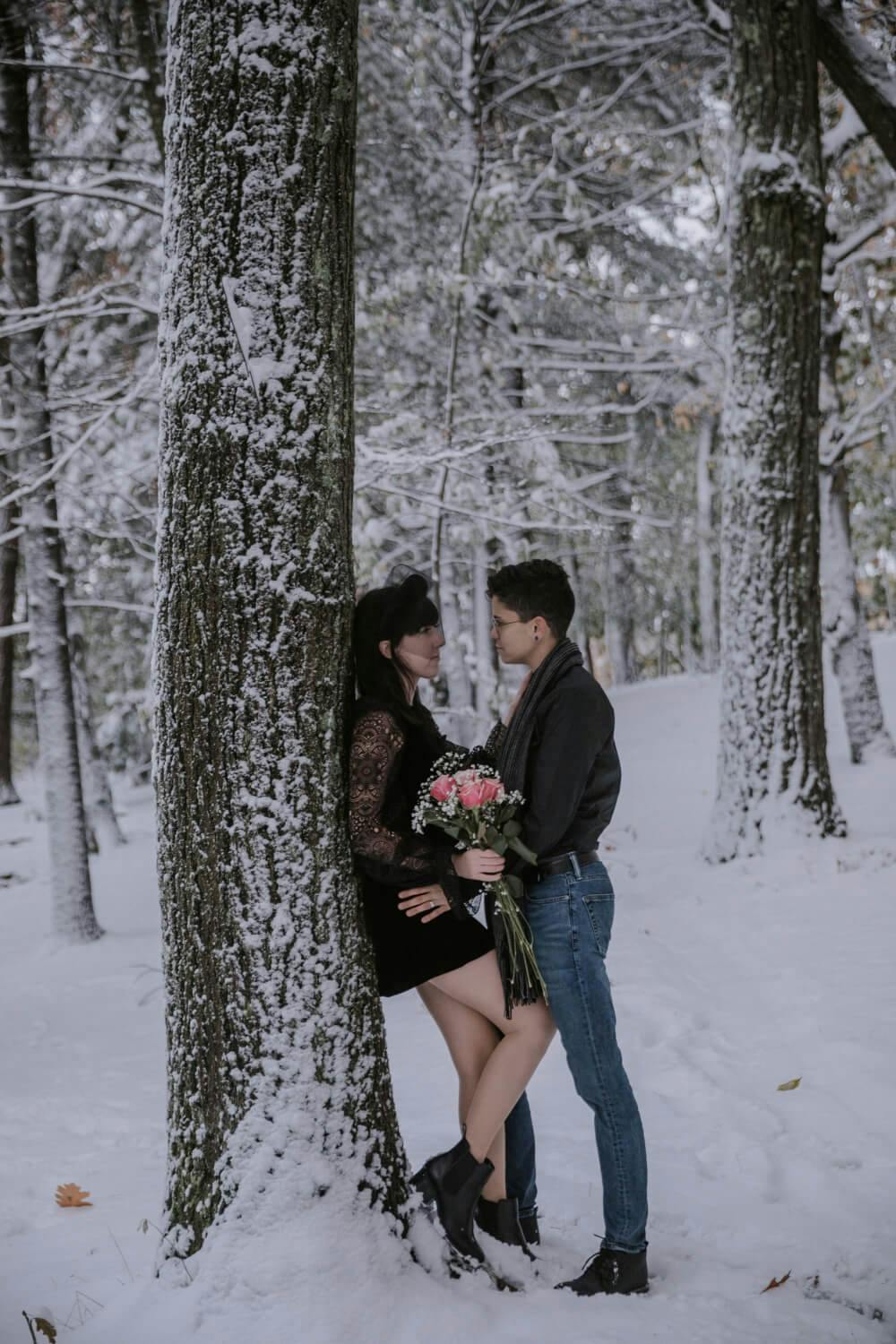 A couple embracing by a tree in a snowy forest