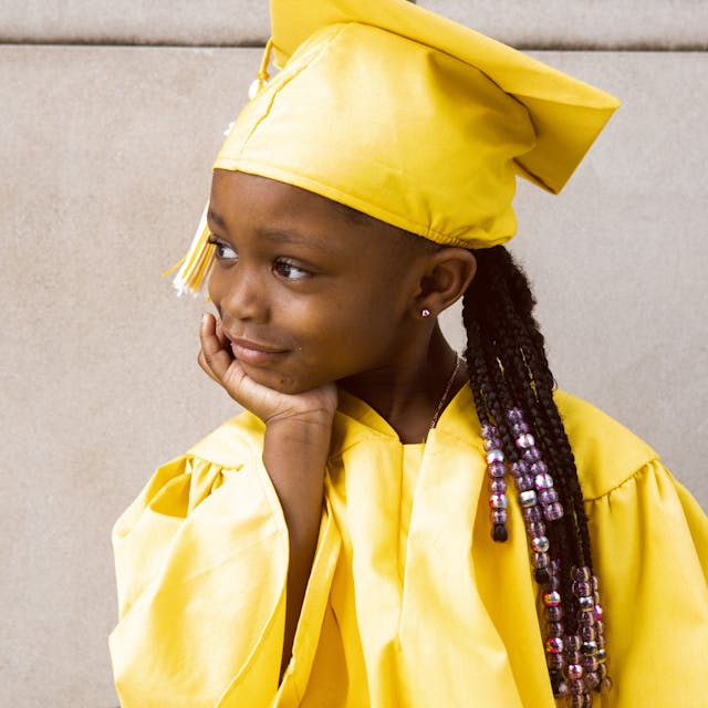 A young girl in a yellow graduation gown and cap looking thoughtful.