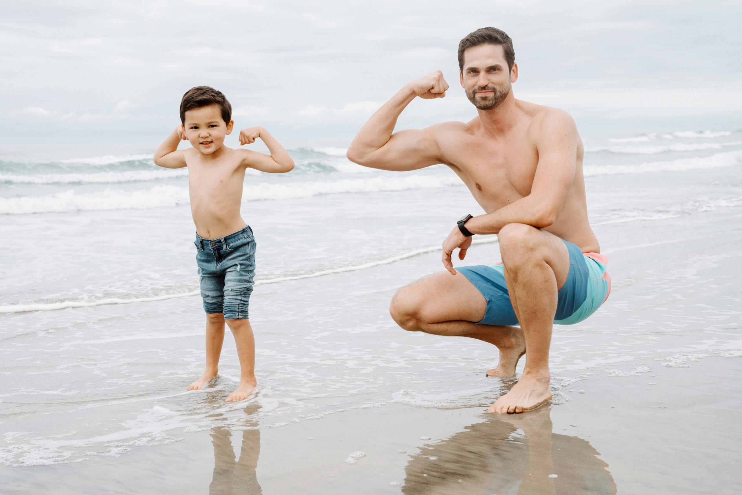 A young boy and a man flexing their muscles on the beach