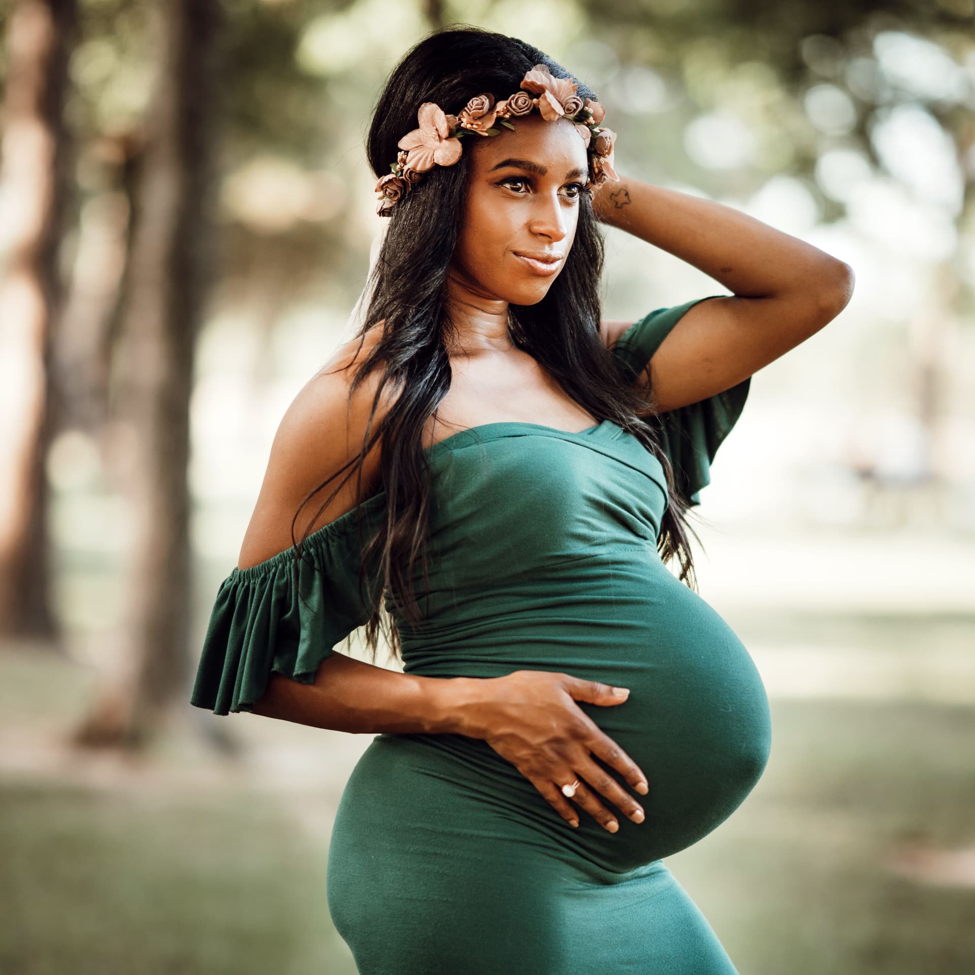 Pregnant woman wearing a green dress and flower crown smiles for her free outdoor maternity photoshoot