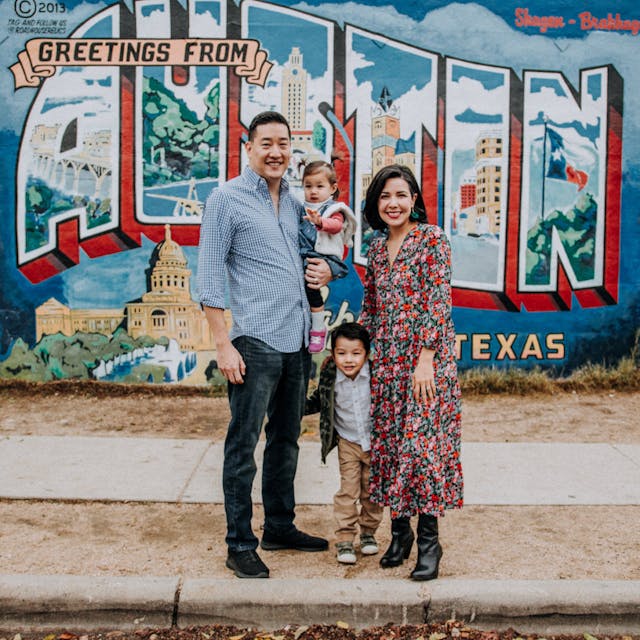 A family standing in front of a colorful mural with 'Greetings from Austin Texas' written on it.