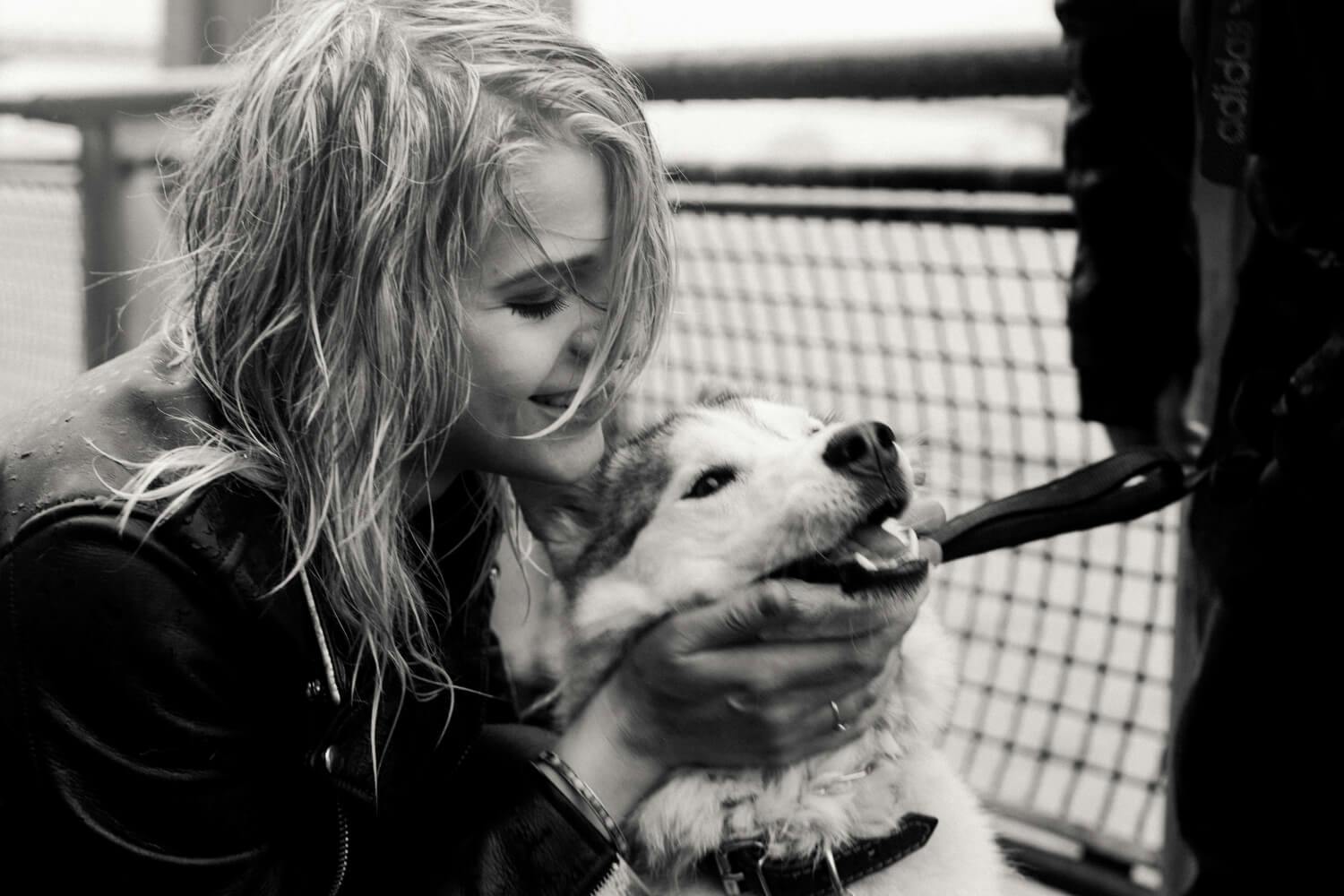 A young woman bending down to pet a smiling dog in a black and white photo