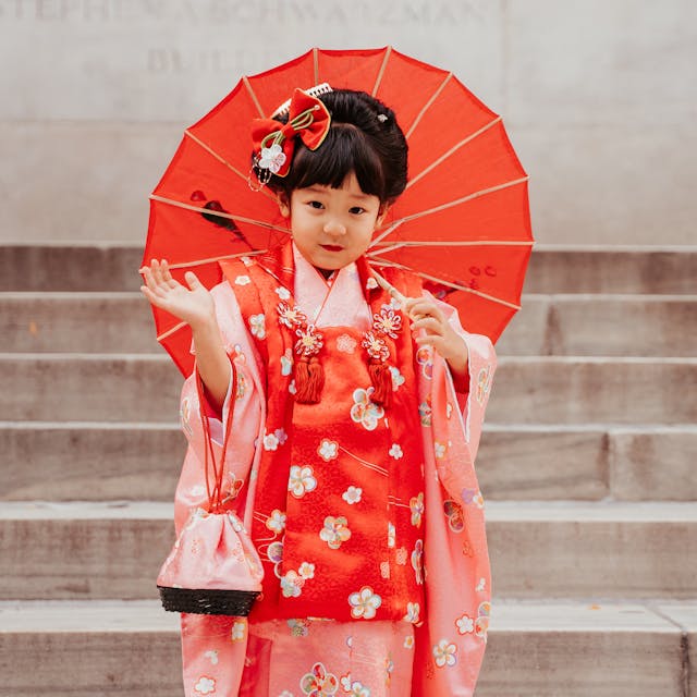 A young girl in a red kimono holding a red umbrella on stairs.