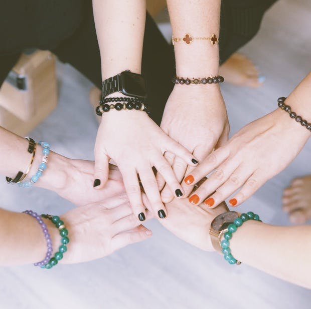 A group of people with various bracelets stacking hands in a show of unity or friendship.