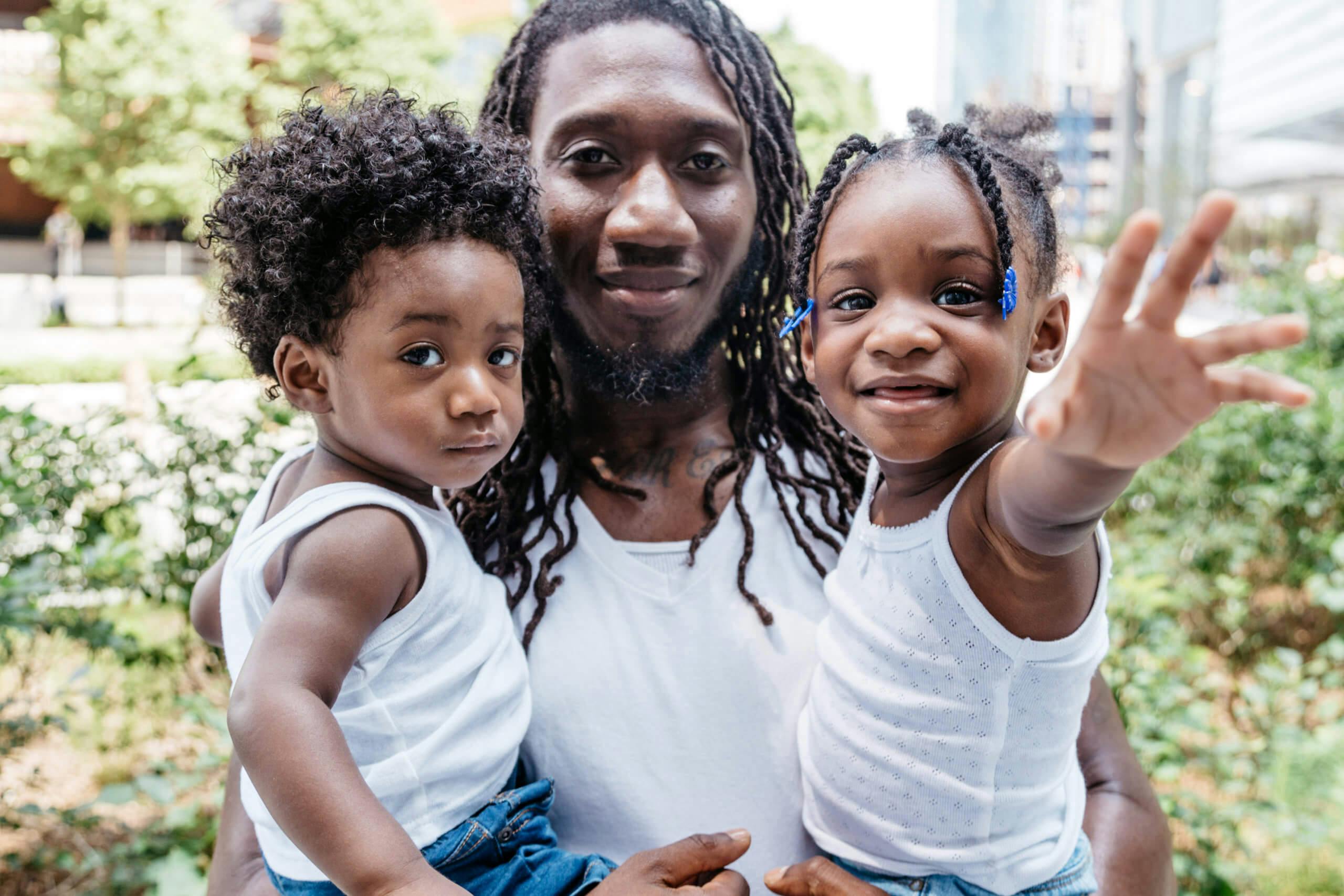 A man with long dreadlocks holding two young children