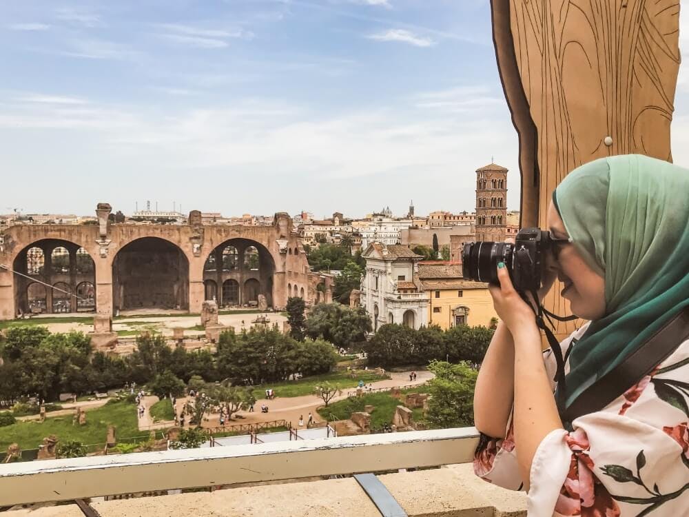 A woman in a hijab taking photos with a camera overlooking ancient Roman ruins