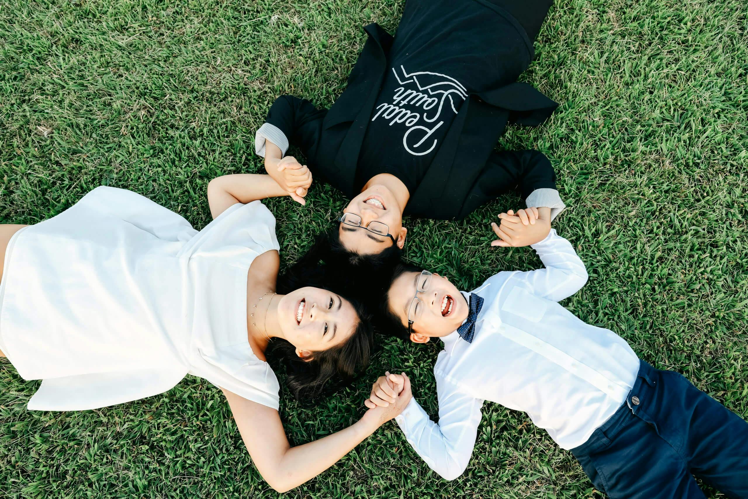 Three people lying on grass and holding hands, looking upwards