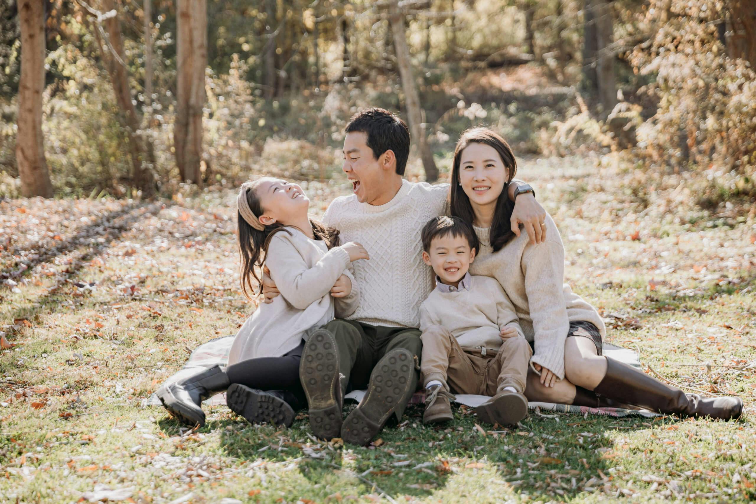 A happy family of four sitting on the grass in a sunny autumn park