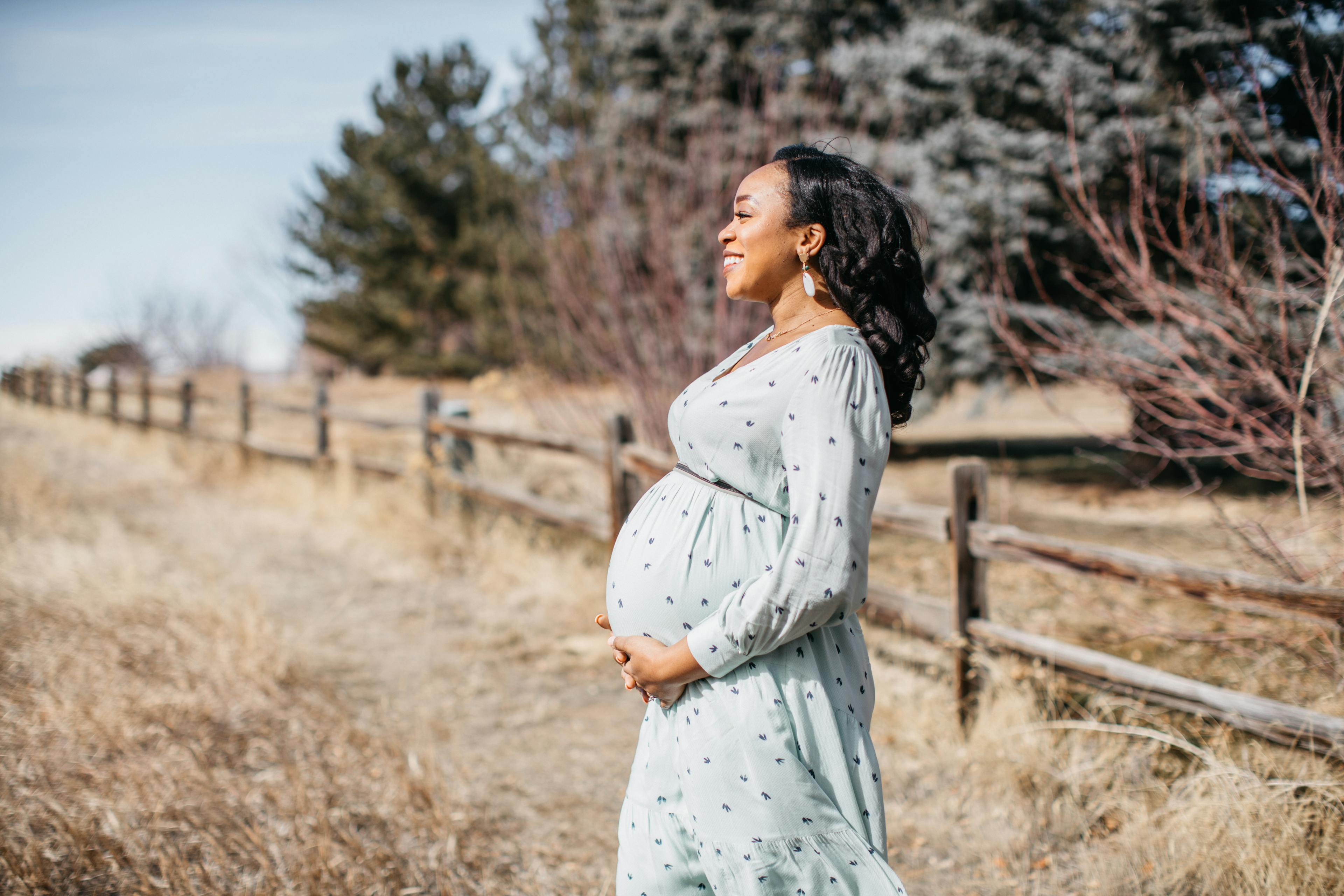 Pregnant woman smiling in a field next to a wooden fence