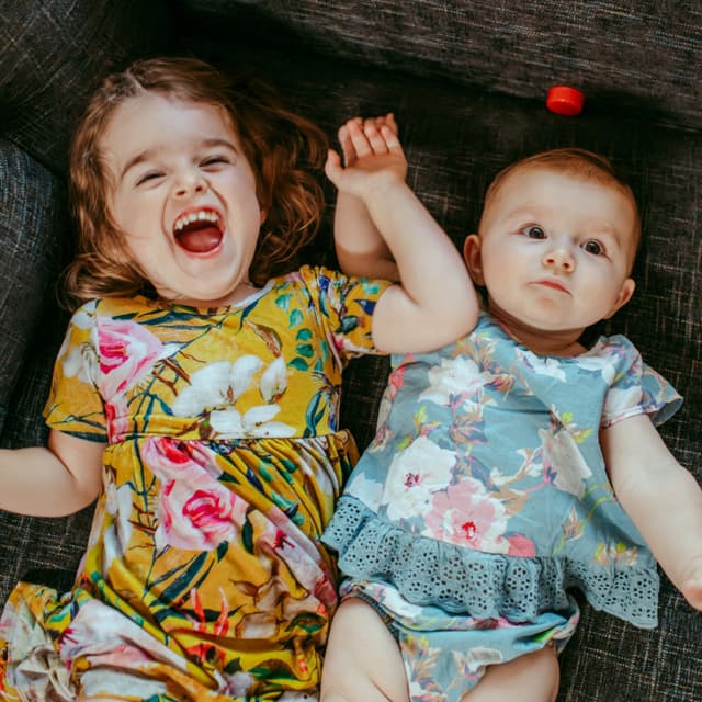 Two children lying on a couch, one laughing and one looking at the camera