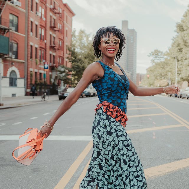 Fashionable woman dancing on a city street with a bright orange handbag