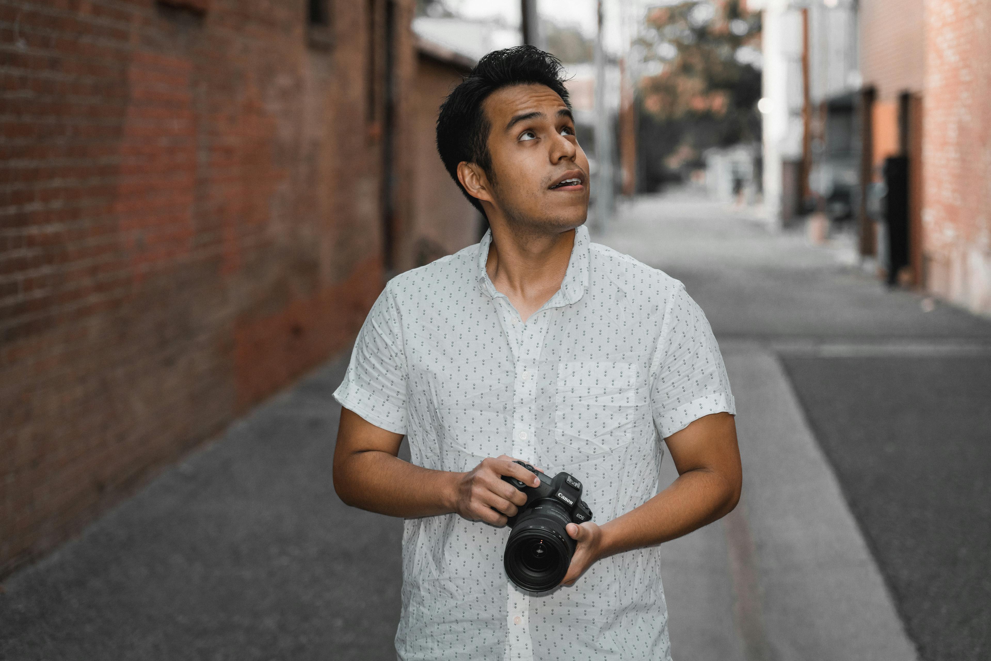 Pensive young man with a camera standing in an urban alley.