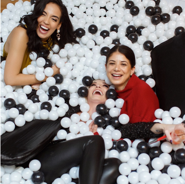 Three women smiling and having fun in a ball pit with black and white balls.