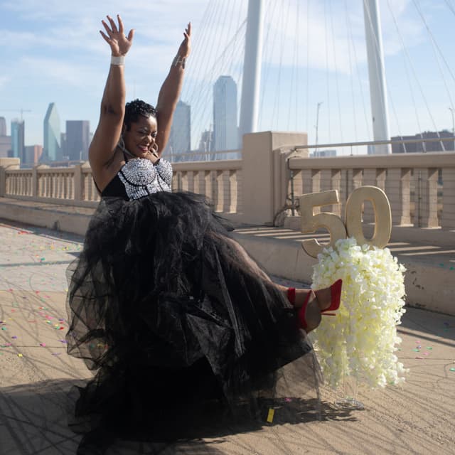 Woman celebrating with arms raised next to a '50' golden balloon on a bridge