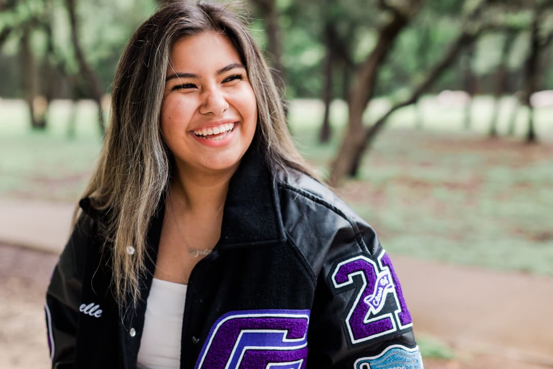 Smiling young woman wearing a letterman jacket outdoors