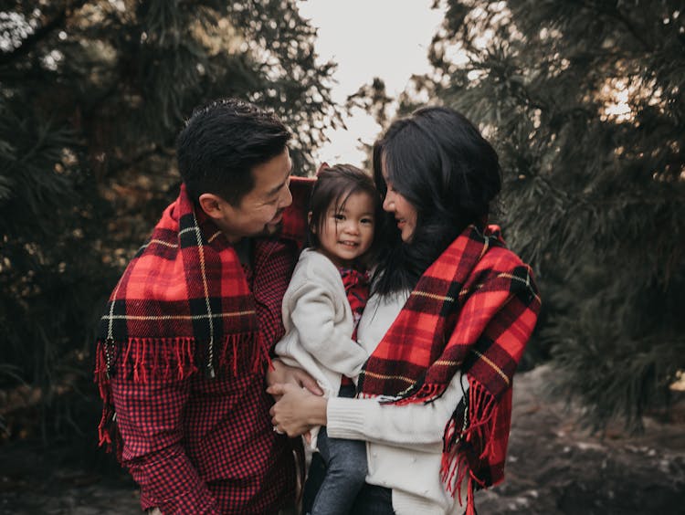 A happy family with a child wrapped in a red plaid blanket standing in a forest.