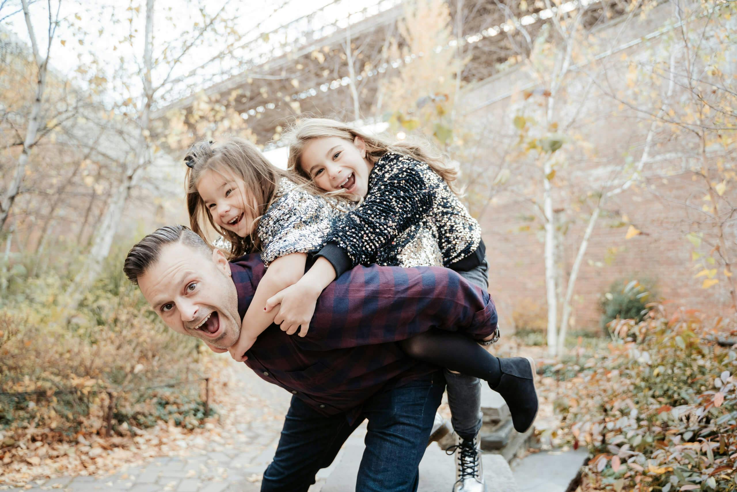 A man giving two young girls piggyback rides in a playful autumn setting