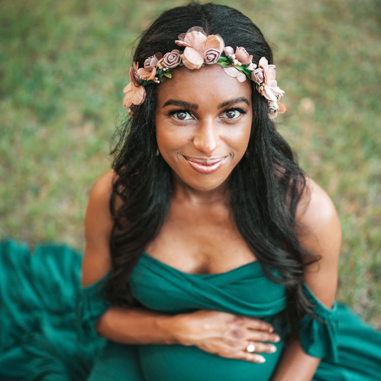 Pregnant woman wearing a green dress and flower crown smiles for her free outdoor maternity photoshoot