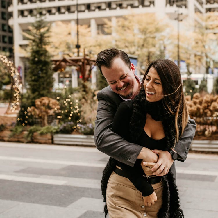 Laughing couple hugging and dancing on a city street with holiday decorations