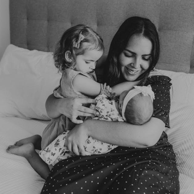 Black and white image of a woman cuddling with her young daughter and infant