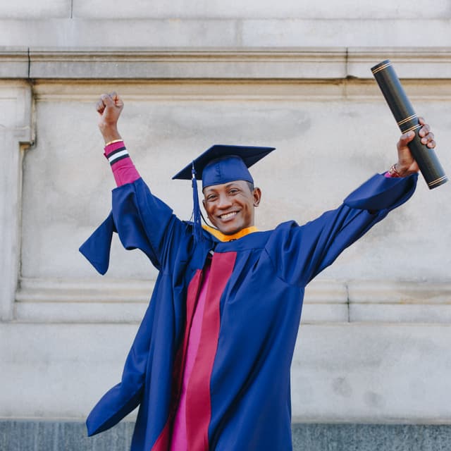 Graduate in cap and gown holding a diploma and celebrating.