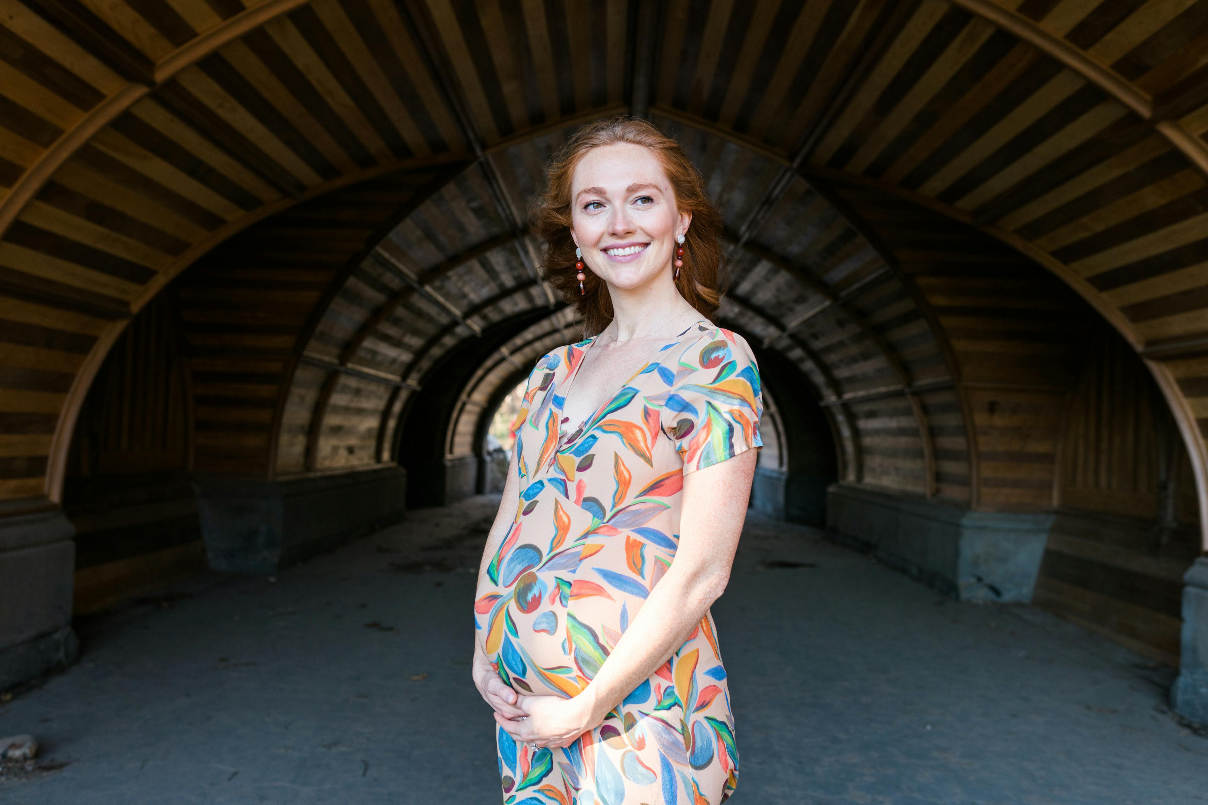 A radiant pregnant woman in a colorful dress smiling in an arched tunnel